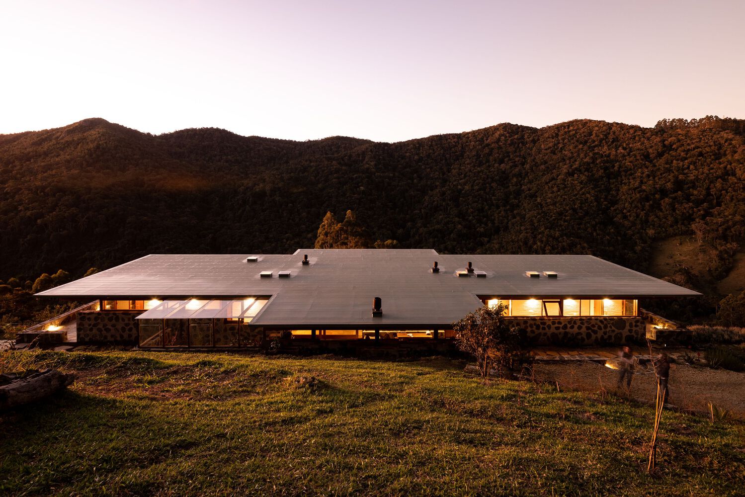 Casa 23.44 iluminada ao entardecer, cercada pela Serra da Bocaina